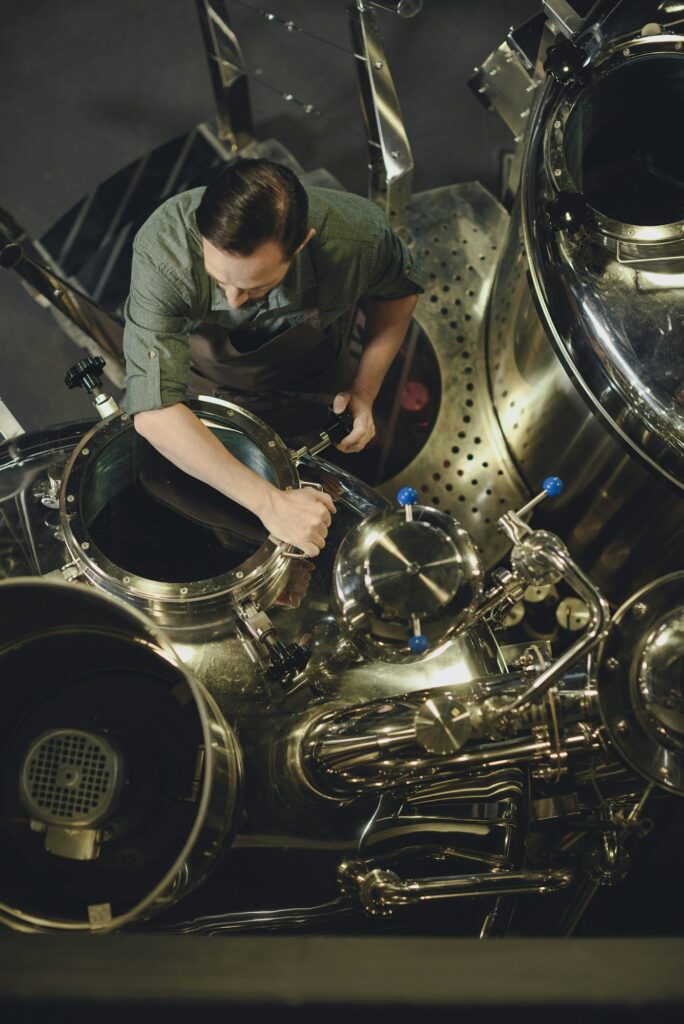 Overhead view of male brewer in apron inspecting tank at the brewery